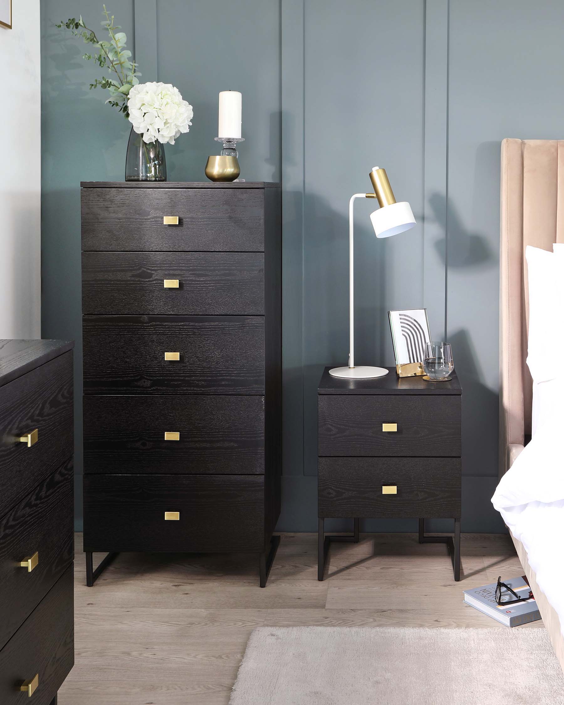 A contemporary bedroom set featuring a tall, dark wooden dresser with five drawers accented by brass handles, and a smaller, matching three-drawer nightstand with brass details. Both stand on slender, tapered legs.