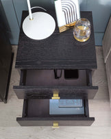 Contemporary black nightstand with textured finish, featuring two open drawers showcasing elegant golden handles, set against a light wooden floor.