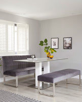 A sleek glass-top dining table with modern white and silver legs, paired with plush, gray upholstered benches.