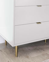 Modern white chest of drawers with sleek horizontal lines and brass-finished metal handles and legs.