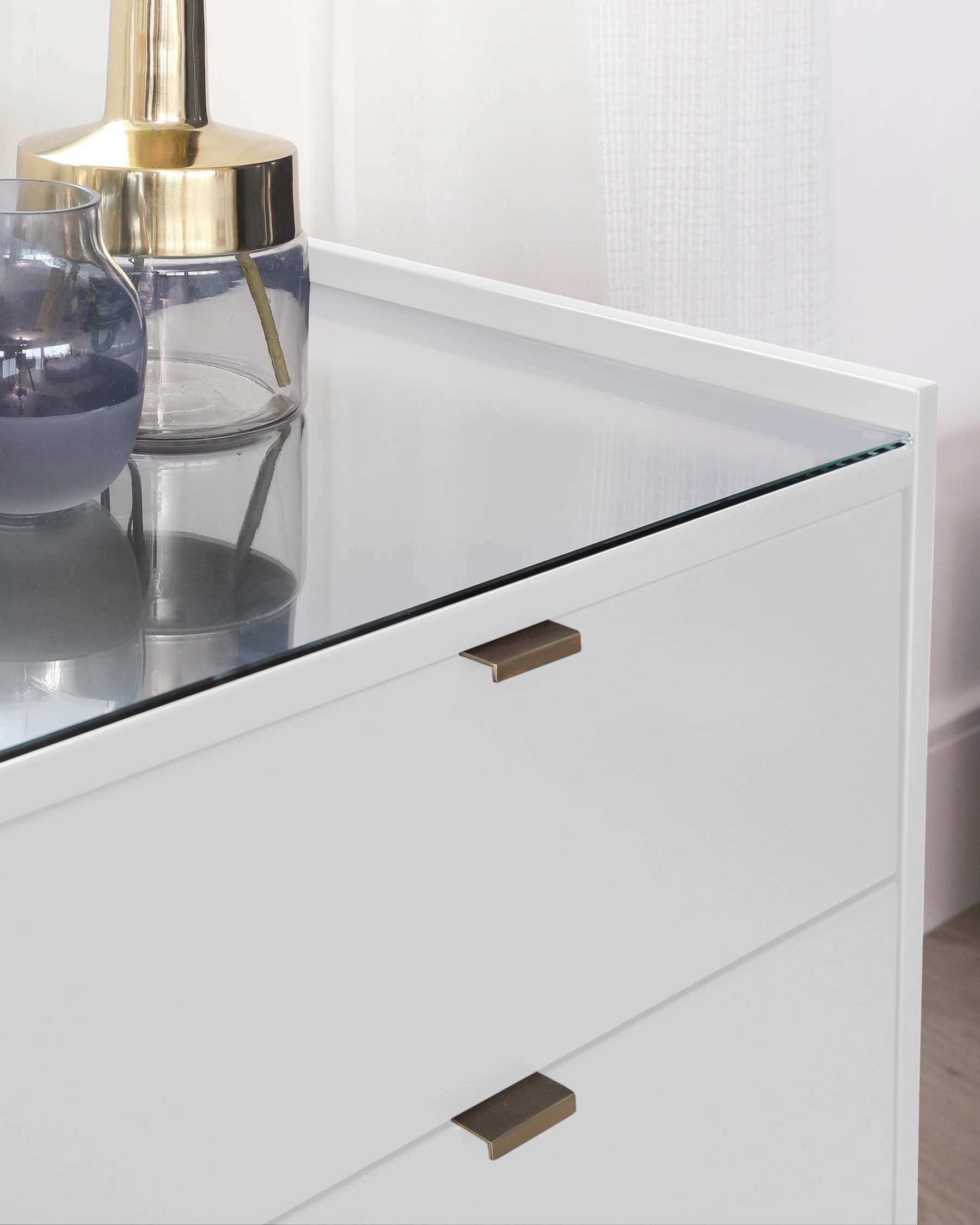 Modern white dresser with a glossy finish and clear glass top, featuring sleek drawer handles in a brushed metal finish.