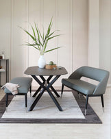 Contemporary round dark table with a unique X-base design, alongside a modern grey upholstered chair with sleek lines and metal-tipped legs. A smaller stool with a matching design complements the set. Positioned on a two-tone area rug, this setup creates a sophisticated and stylish look.