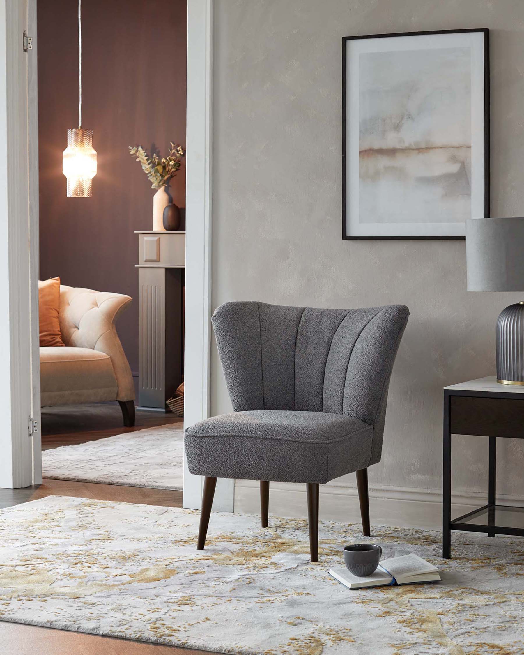 Elegant grey fabric wingback accent chair with tufted backrest and dark wooden legs, beside a black metal side table with a modern table lamp. A decorative cream rug with yellow and grey accents covers the floor.