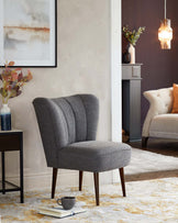 Elegant contemporary living room furniture ensemble featuring a grey wingback chair with vertical channel tufting and tapered wooden legs, a beige tufted armchair with a curved back and plush cushions, and a simple black side table with a rectangular top and slender legs. Both chairs are adorned with stylish throw pillows, and the scene is anchored by a cream and yellow patterned area rug. Decorative lighting and a framed abstract artwork add a touch of modern sophistication to the setting.