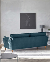 Elegant three-seater sofa with velvety teal upholstery and tapered wooden legs, featuring plush back cushions and a single flange edge detail, accompanied by a minimalist round side table with a matte black top and slender metallic legs.