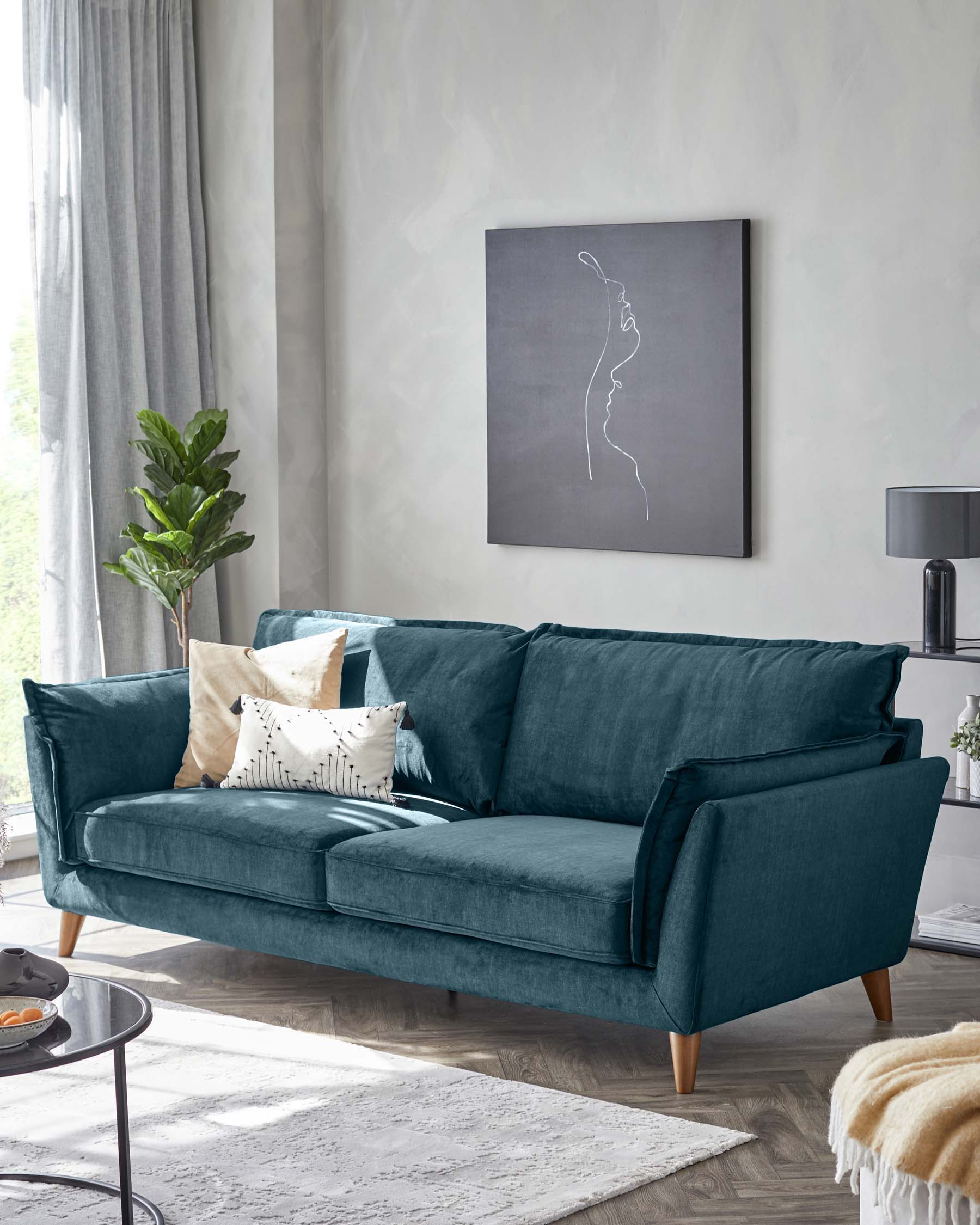 Elegant three-seat sofa upholstered in a plush teal velvet, featuring a clean-lined silhouette with structured arms and back cushions, complemented by three decorative throw pillows in coordinating colours. The sofa stands on tapered wooden legs, set within a modern living room setting with neutral tones.