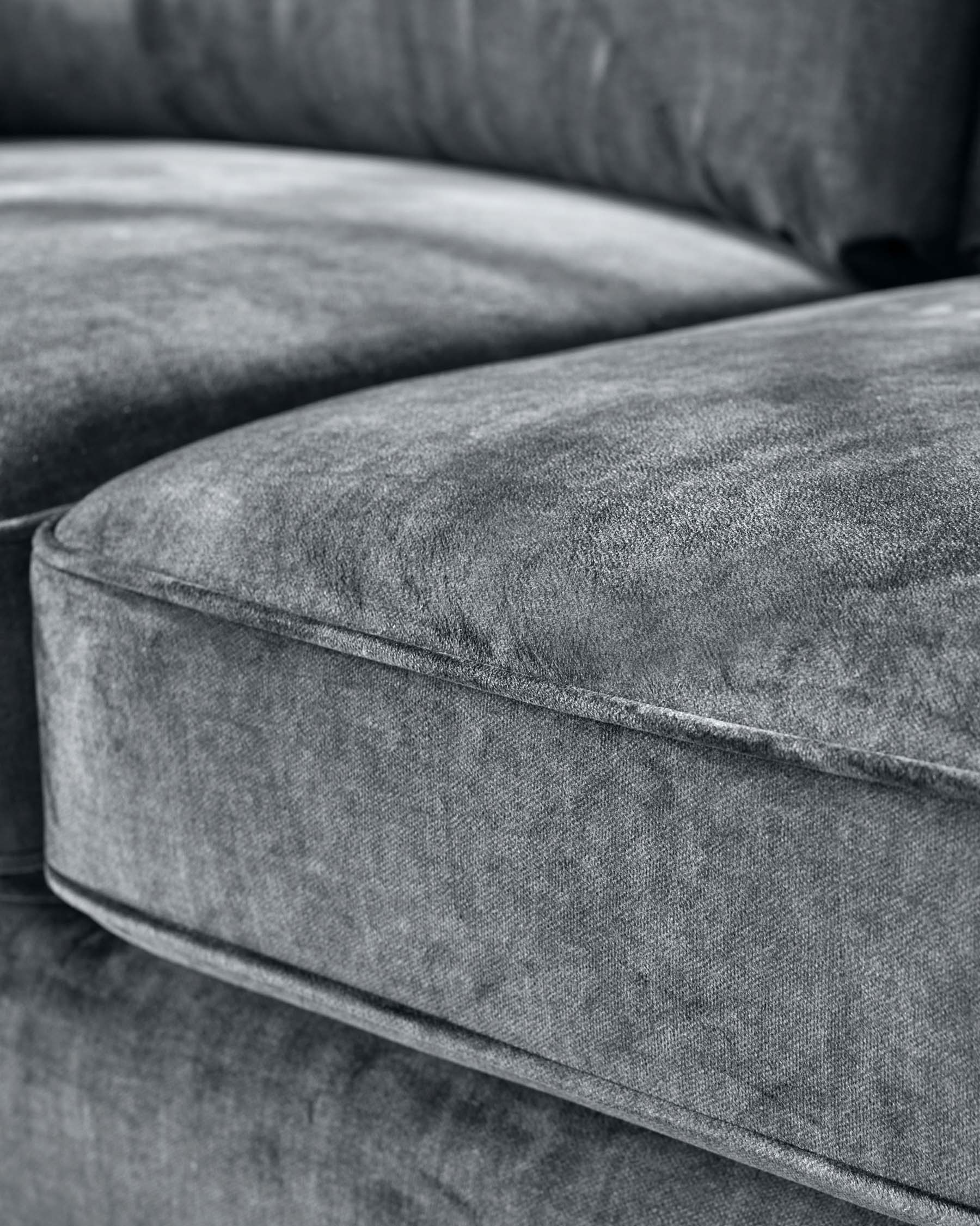 Close-up of a section of a grey upholstered sofa, showcasing plush velvet fabric and soft cushioning in monochrome tones.