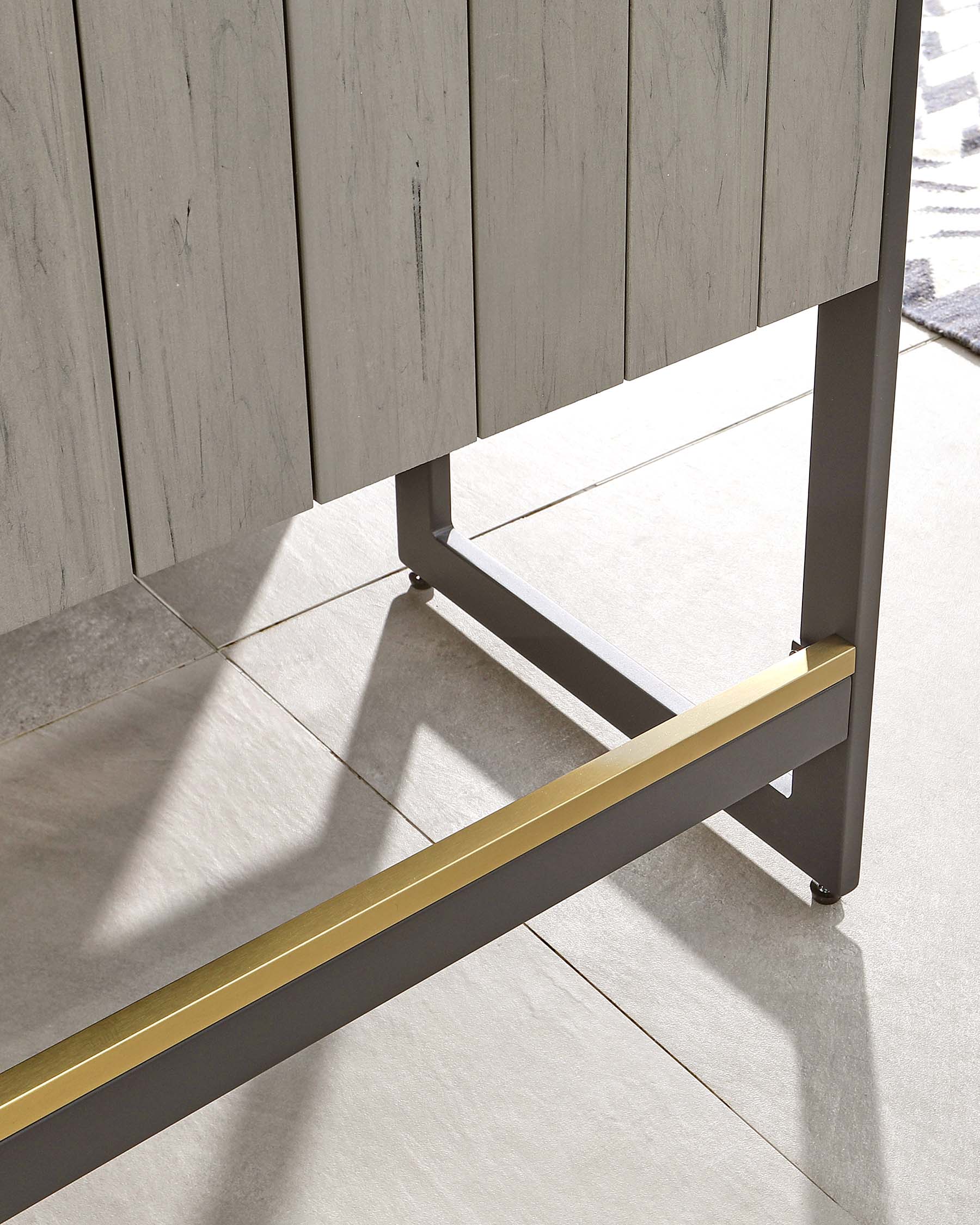 Modern minimalist table with a grey wooden top and a sturdy metallic base featuring distinctive brass-coloured horizontal accents.