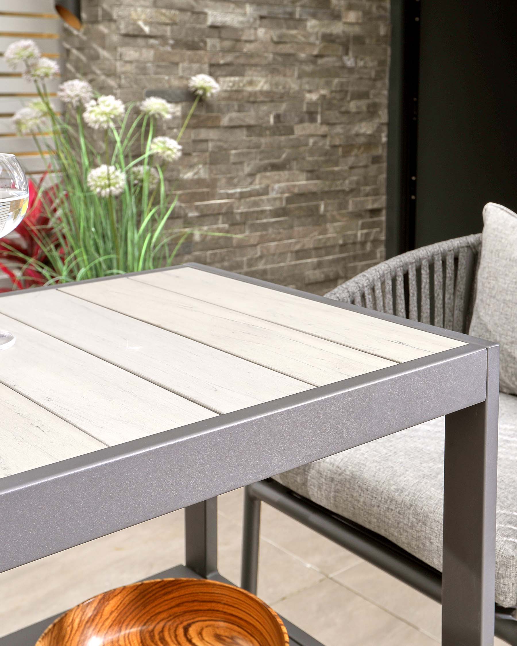 A modern outdoor table with a slatted top, metal frame, and a cozy grey upholstered chair paired with a wooden bowl.