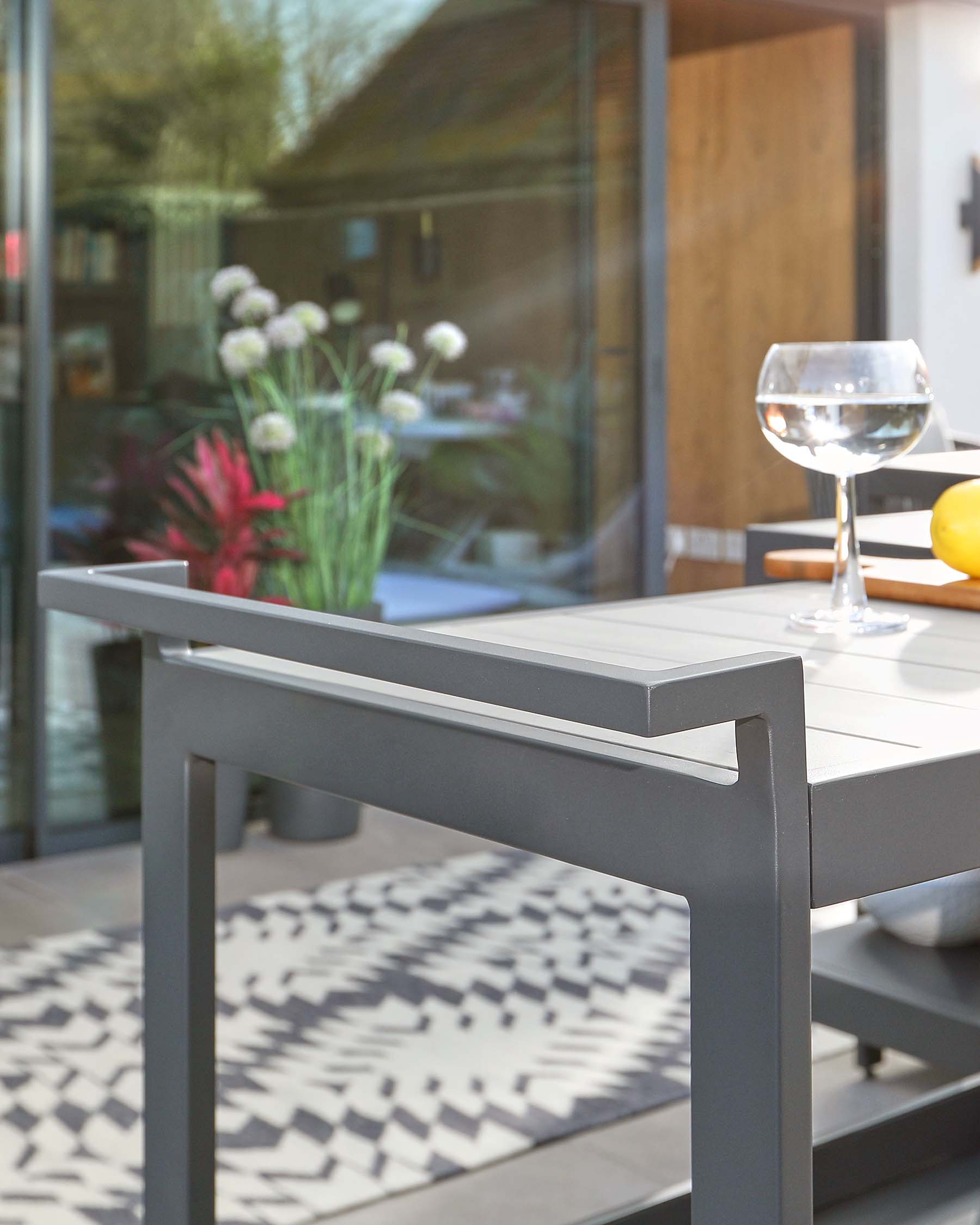 Modern outdoor dining furniture set featuring a sleek grey table with a solid, minimalist design and matching chairs, complemented by a patterned rug; all bathed in natural light, indicative of a contemporary alfresco dining experience.