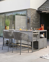 Modern outdoor bar with two stylish gray wicker stools, a sleek countertop, and elegant glassware for entertaining.