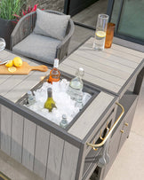 Stylish outdoor furniture featuring a gray cushioned chair, a bar cart with an ice compartment, and elegant drinkware.