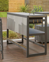 Modern outdoor charcoal grey bar unit with clean lines, featuring a brushed metal frame, an integrated footrest, a smooth countertop, spacious open shelving, and golden accents on the handles and footrest.