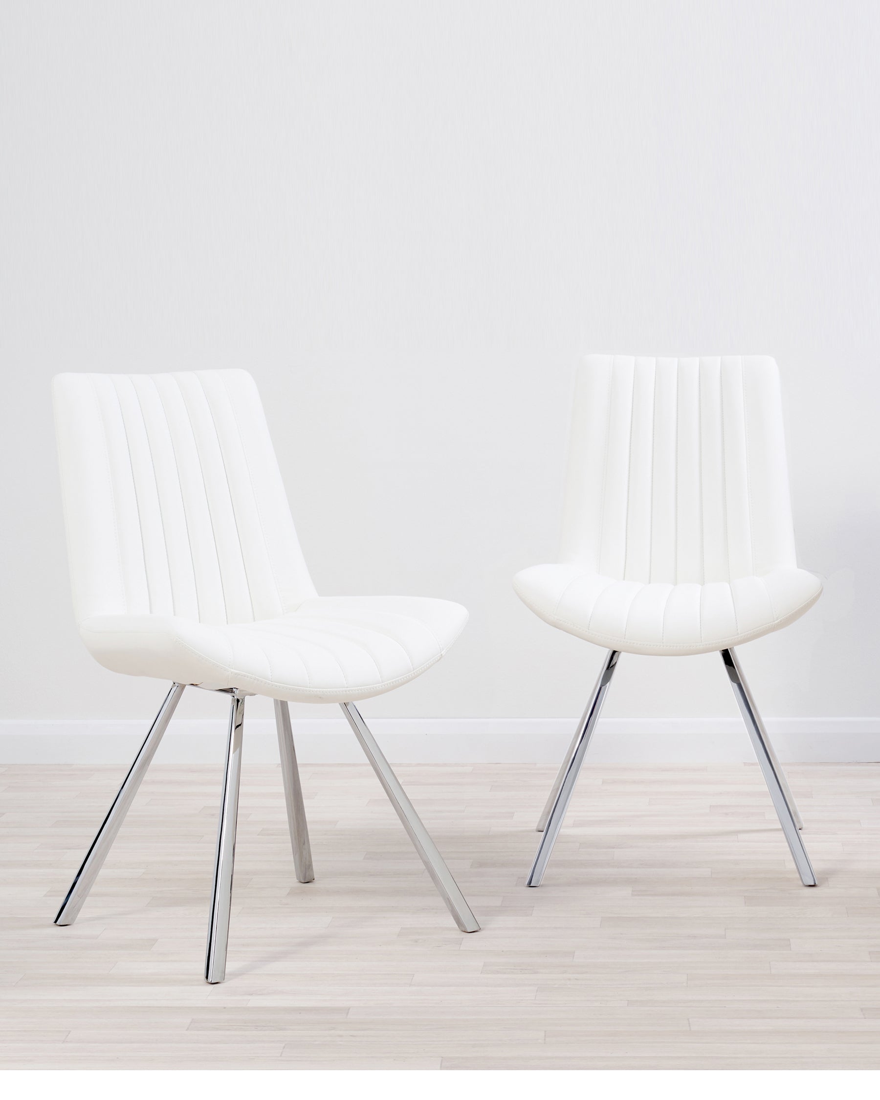 Two contemporary white upholstered dining chairs with vertical stitching detail on the backrest and seat cushion, set on sleek, angled chrome legs.