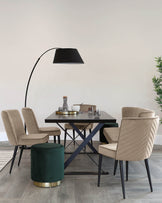 Modern dining set featuring a dark rectangular table with a unique X-shaped metallic base and three upholstered chairs with a vertical stitch pattern and slender black legs. A green velvet ottoman with a gold metal base adds a touch of luxury. An elegant arc floor lamp with a large black shade overlooks the setting, creating a sophisticated ambiance.