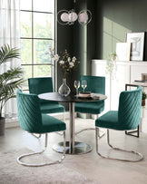 A sleek black round table surrounded by four green velvet chairs with a modern design, complemented by a contemporary light fixture.