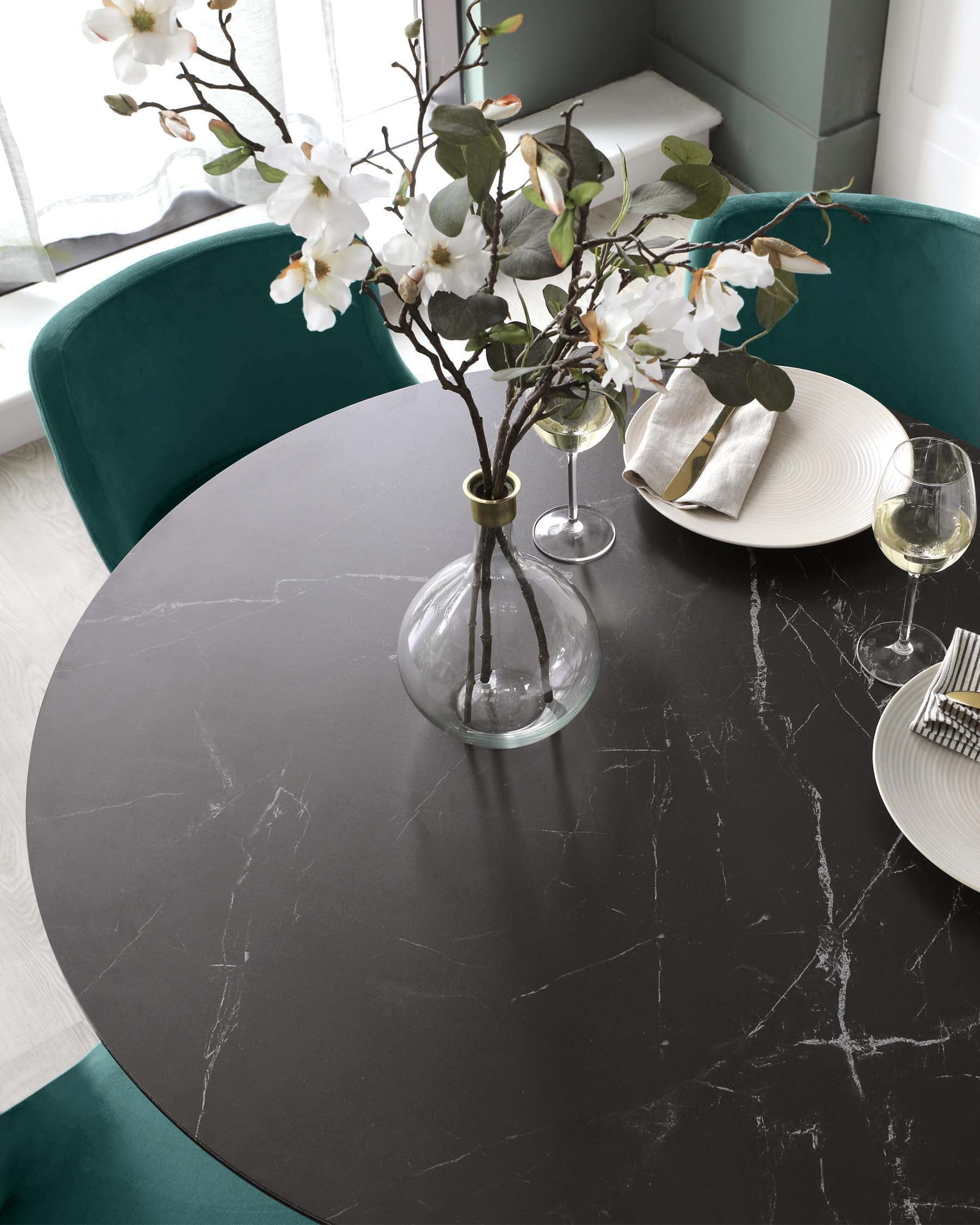 A round black marble table topped with a glass vase of flowers, accompanied by elegant plates, napkins, and wine glasses.