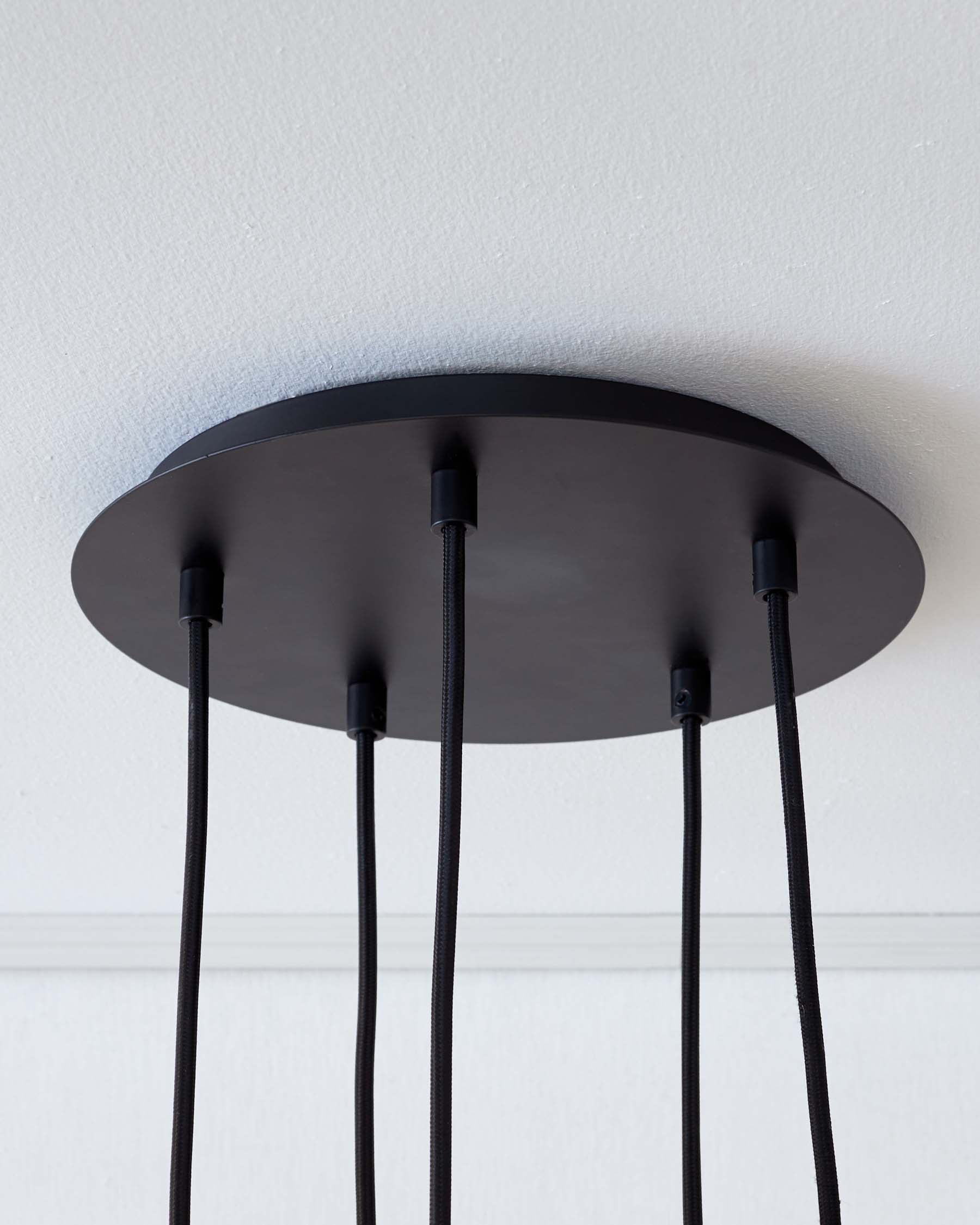 Modern circular black ceiling lamp base affixed to a white wall, with multiple cords hanging straight down.