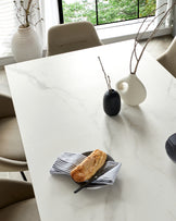 Modern dining room featuring a rectangular marble table with a matte finish, complemented by a set of four upholstered beige dining chairs with a smooth and sleek design. The table is accessorized with a black vase and a white vase, each holding a minimalist branch, adding a touch of elegance to the setting.