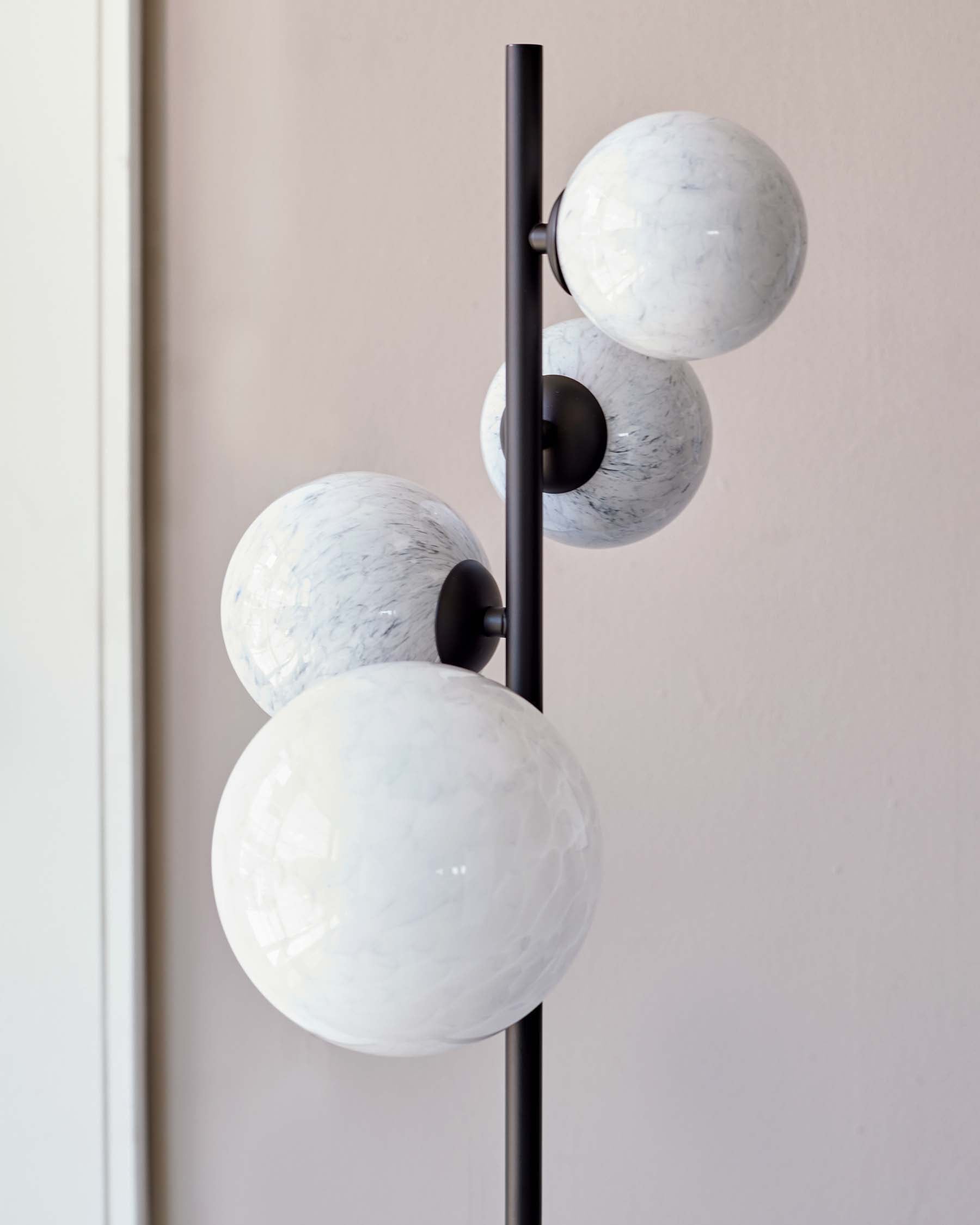 Floor lamp with a vertical black rod supporting three spherical white marble shades at staggered heights against a pale background.