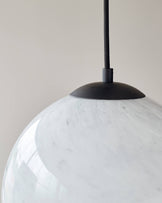 Modern minimalist pendant light with a large, white marble-patterned glass shade and matte black canopy and cable.