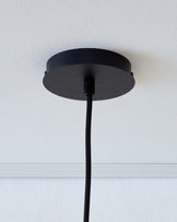 No furniture is depicted; the image shows a close-up of a black pendant light canopy against a white wall with a cord hanging down.