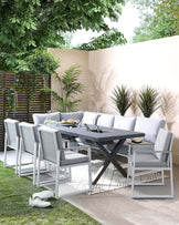 Modern outdoor dining furniture set featuring a rectangular grey table with a cross-leg design and six matching armless chairs with grey cushioned seats and backs, set against a backdrop of greenery and a beige wall, on a patriot with patterned tile flooring.