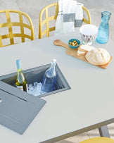 Modern outdoor furniture: a light grey square table with built-in ice bucket and a pair of yellow metal lattice-work chairs.