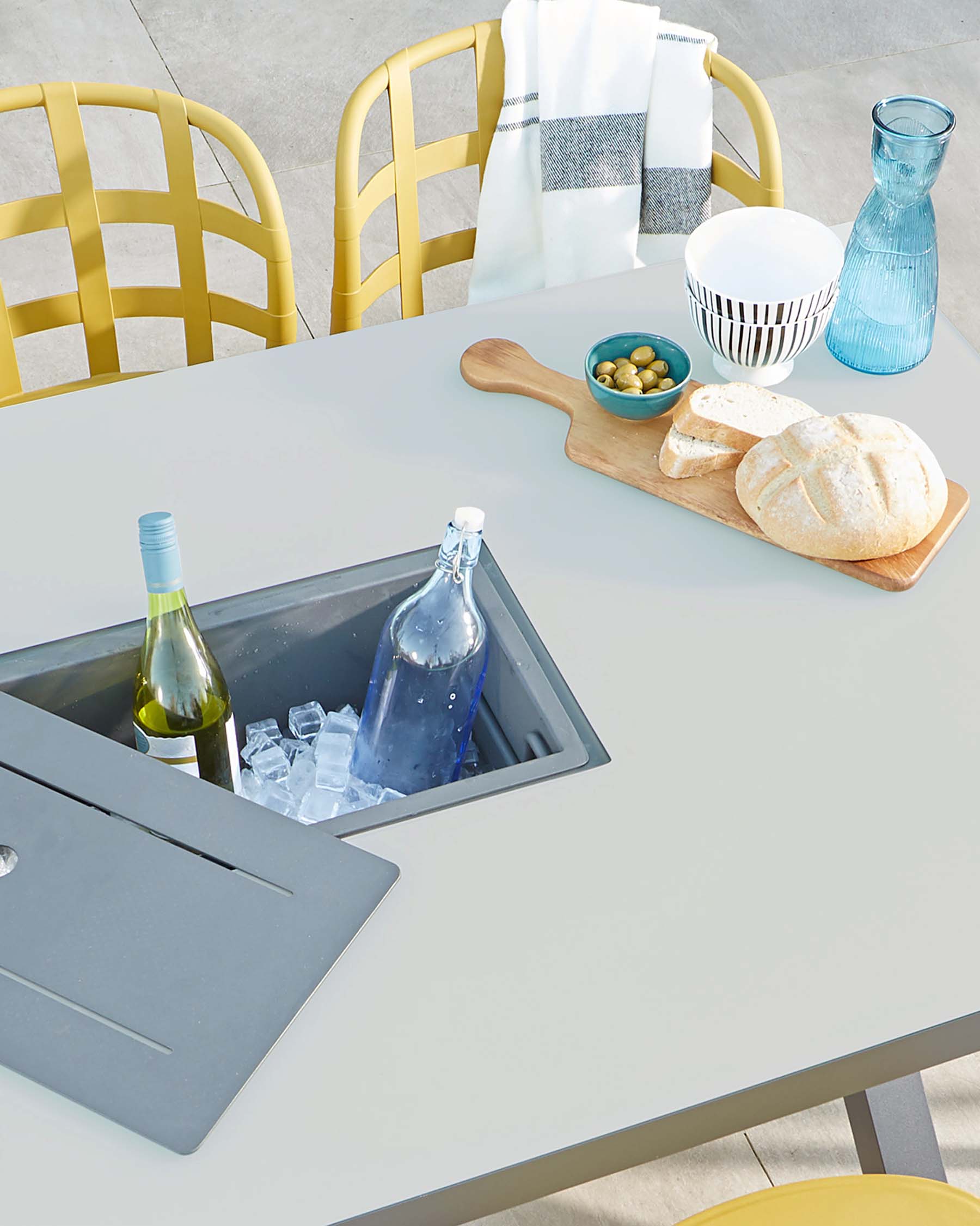 Modern outdoor furniture: a light grey square table with built-in ice bucket and a pair of yellow metal lattice-work chairs.