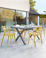 Contemporary outdoor dining set featuring a rectangular table with a smooth grey surface on a unique crisscrossed leg design in a charcoal colour, complemented by four mustard yellow chairs with an open back and curved design.