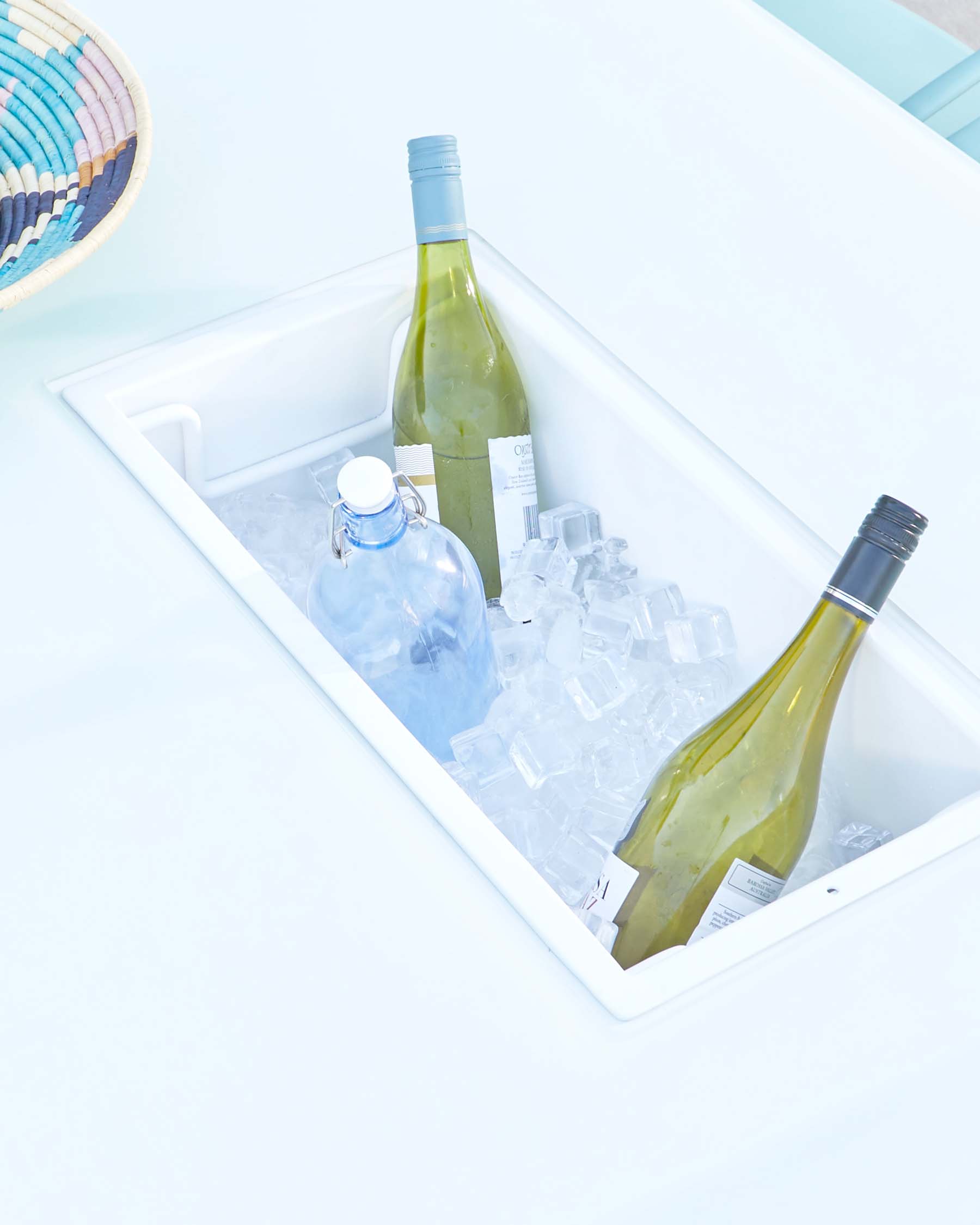 Modern white, built-in outdoor table with an integrated ice bucket feature containing two bottles of wine and ice cubes.