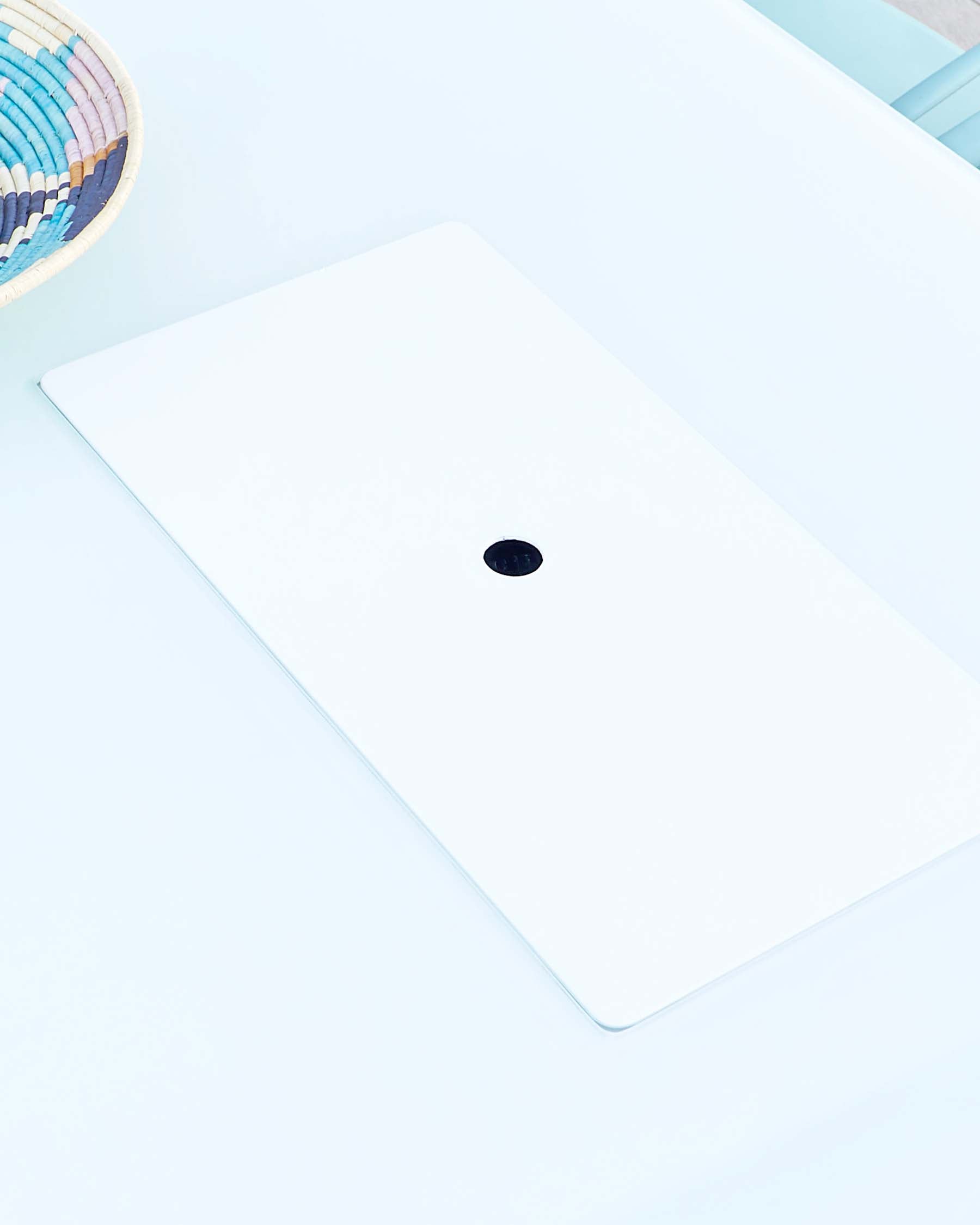 Modern minimalist white desk with a clean design and a single centralized cable management hole, set against a pale blue backdrop.