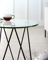 Round glass top side table with slender black metal legs.