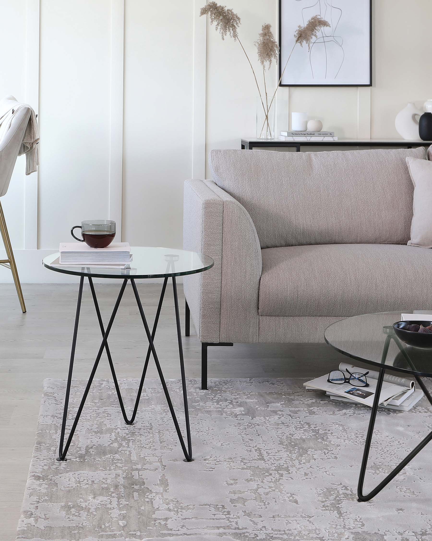 Modern living room with a minimalist beige fabric sofa and two round glass-top side tables with black metal legs, set on a light grey patterned area rug.