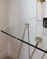 Elegant modern side table with a transparent glass top and a geometric gold-finished metal base.