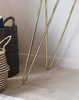 Elegant slim brass-finished metal table legs in a room with light hardwood flooring.