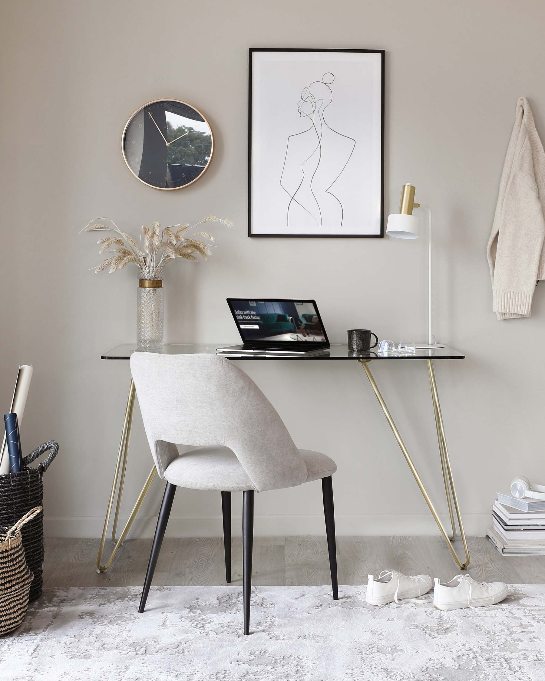 A contemporary home office setup featuring a sleek black desk with a glossy finish and brass-coloured metal legs that form an elegant V shape. Accompanied by a light grey upholstered chair with a curved backrest and black tapered legs, providing a comfortable and stylish seating option. The furniture ensemble creates a modern and sophisticated atmosphere.