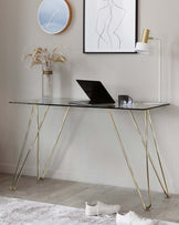 Elegant modern desk with a glass top and slender gold-coloured metal legs elegantly curved into an inverted V-shape.