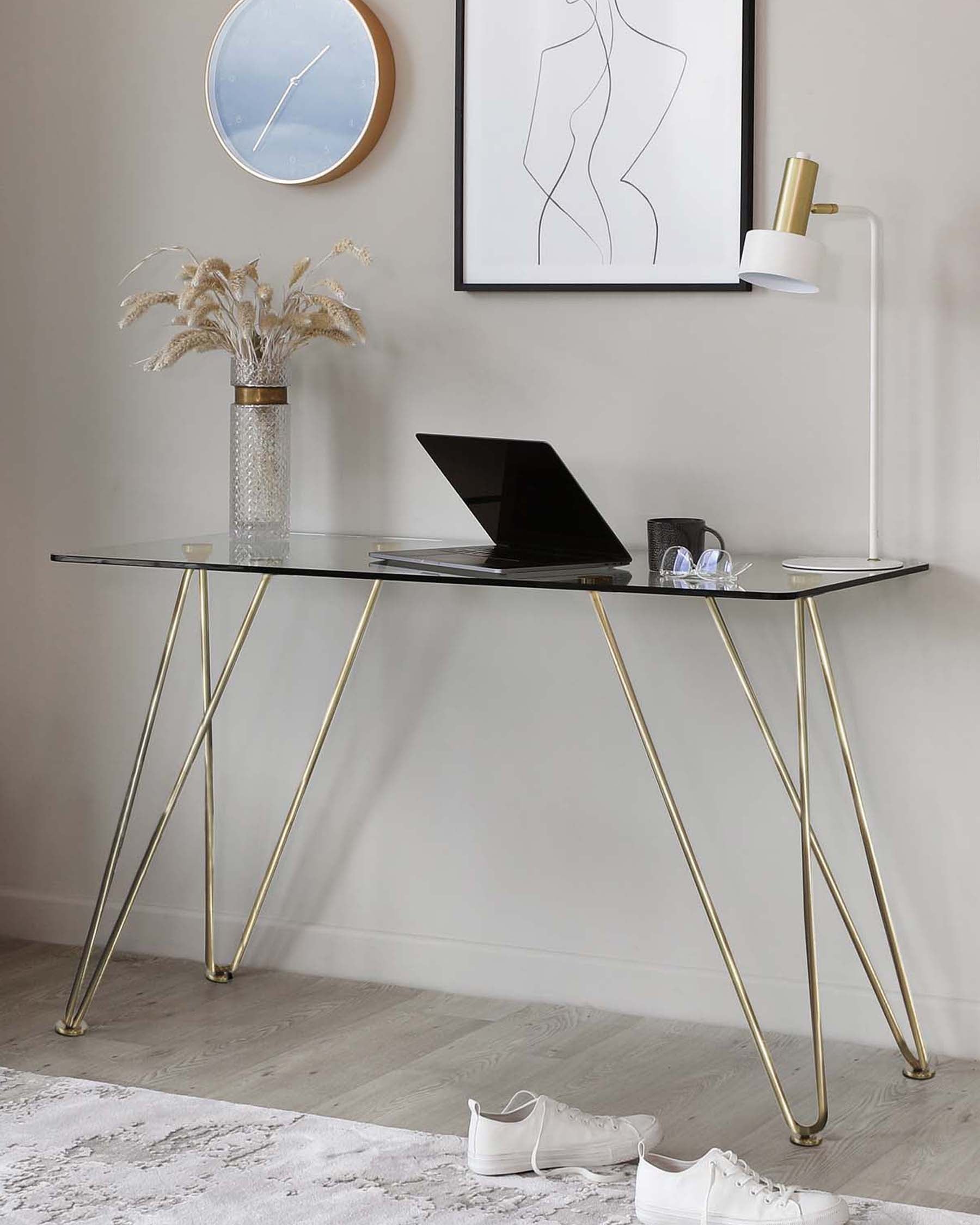 Elegant modern desk with a glass top and slender gold-coloured metal legs elegantly curved into an inverted V-shape.