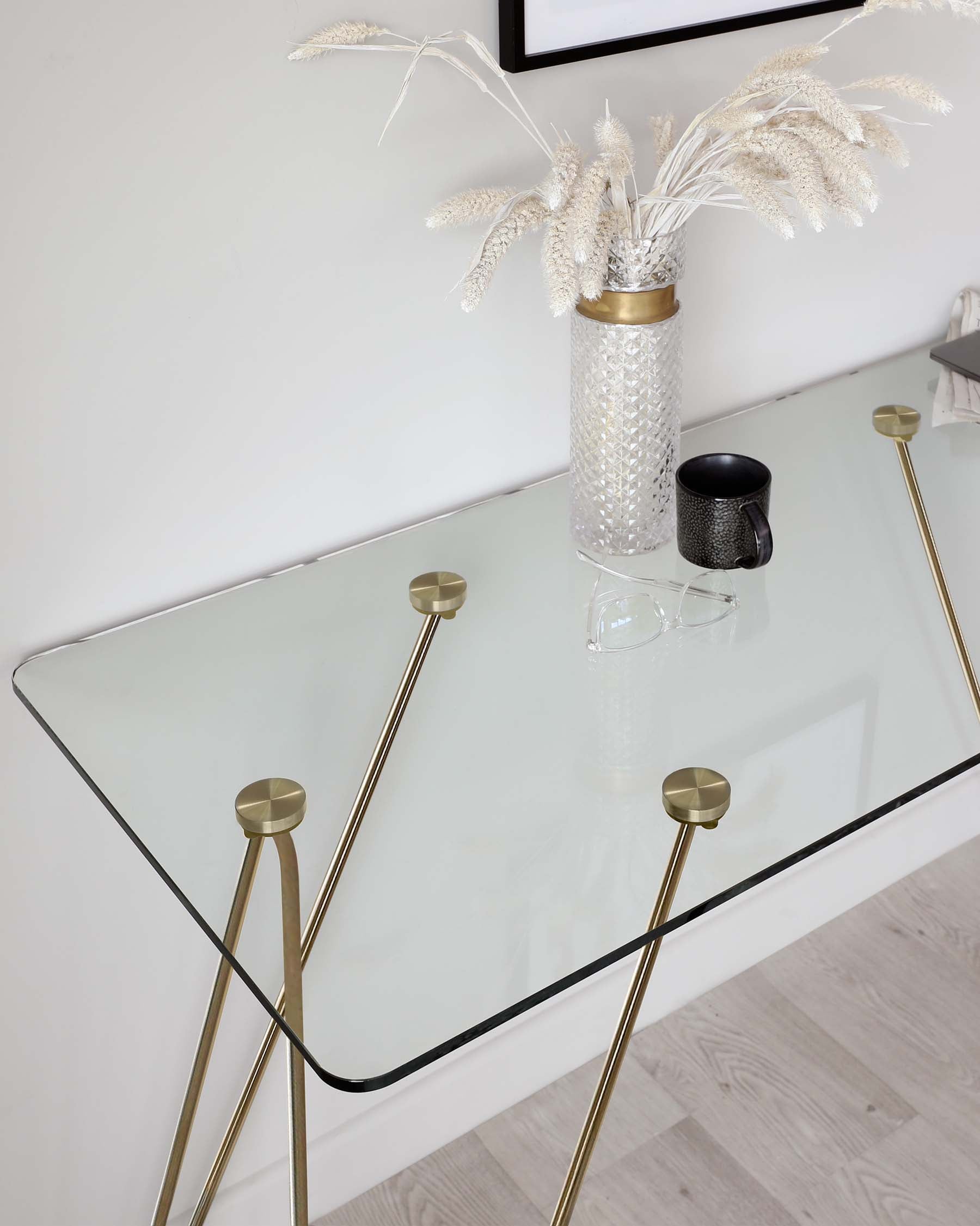 Elegant modern console table with a clear glass top and unique gold-toned metallic legs, featuring spherical accents at the junctions where the legs connect to the tabletop.