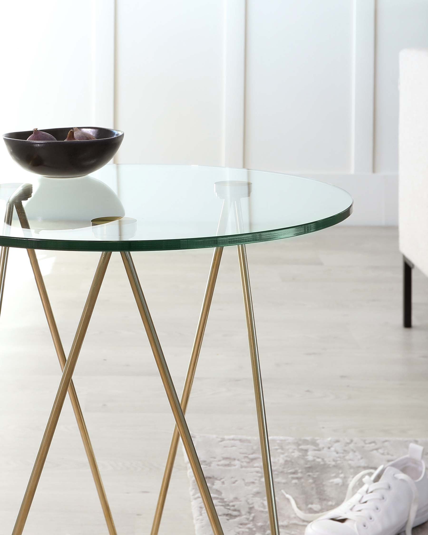 Round glass coffee table with gold-coloured metal legs in a crisscross design.