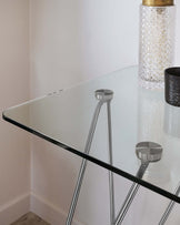 Modern triangular glass-top side table with sleek, chrome-plated tubular steel legs, showcasing a minimalist design suitable for contemporary interiors.