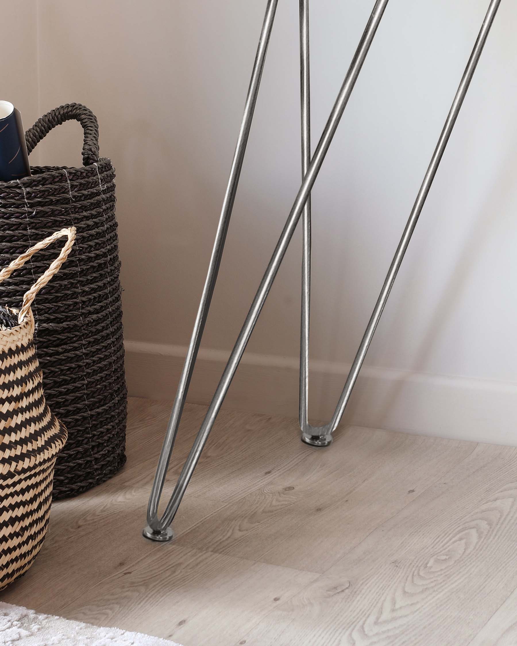 The image shows a section of a piece of furniture with slender, metallic silver legs that angle outwards, culminating in small, round feet resting on a light wooden floor.