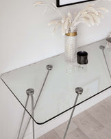 Elegant modern glass console table with a transparent top and a minimalist metal frame with geometric supports.