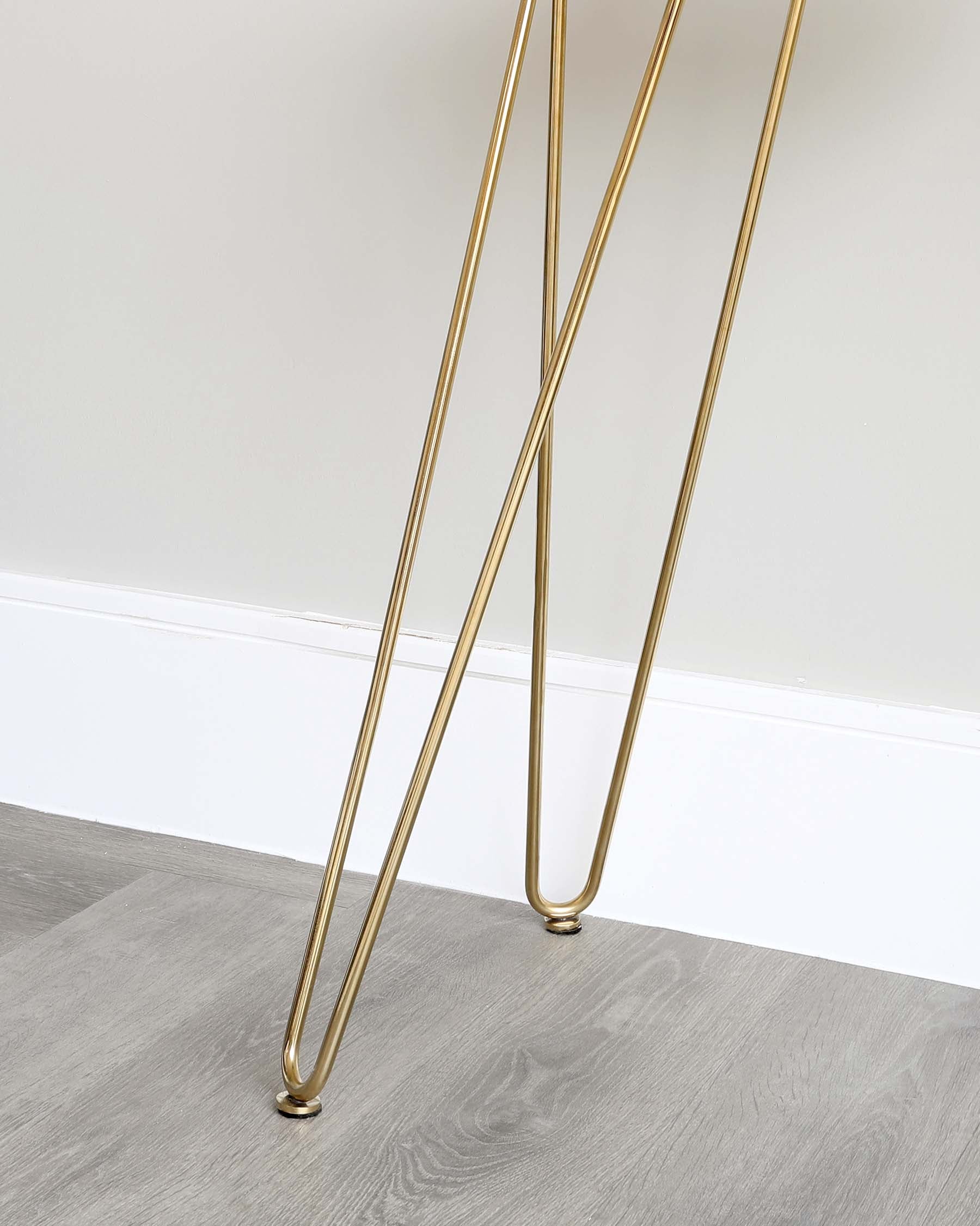 Elegant slim golden metal legs of a piece of furniture against a grey flooring and light wall background.