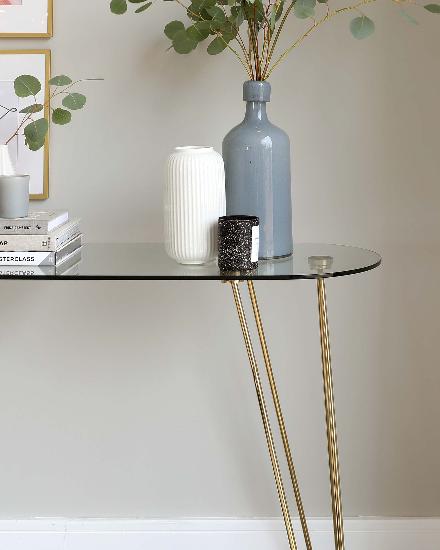 Elegant contemporary console table with a round glass top and slender gold-coloured metal legs.