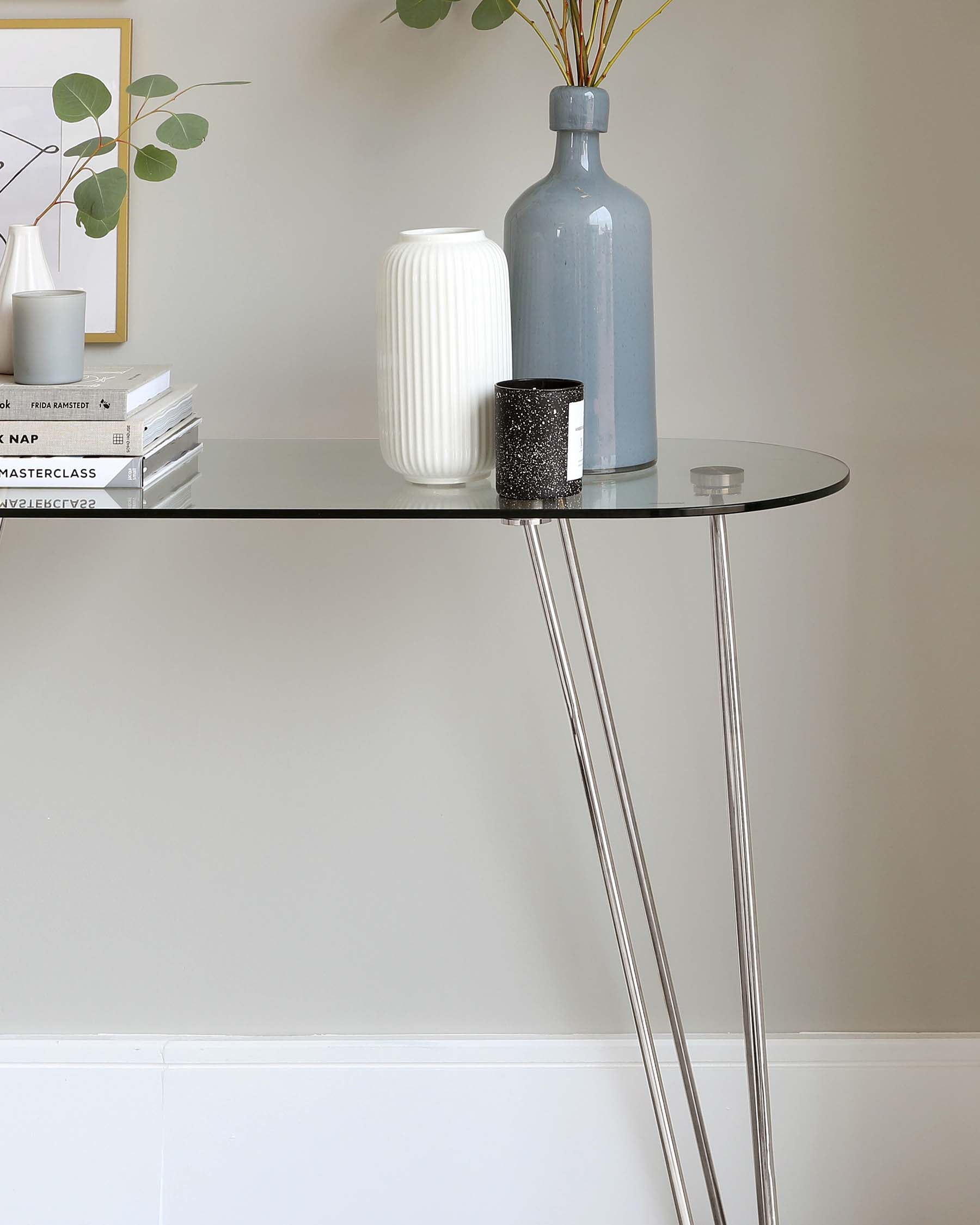 A modern semi-circular console table with a sleek glass top and metallic, slender, crisscrossed legs.