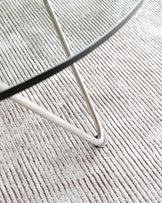 Partial view of a sleek, modern furniture leg with a chrome finish, set against a textured beige carpet.