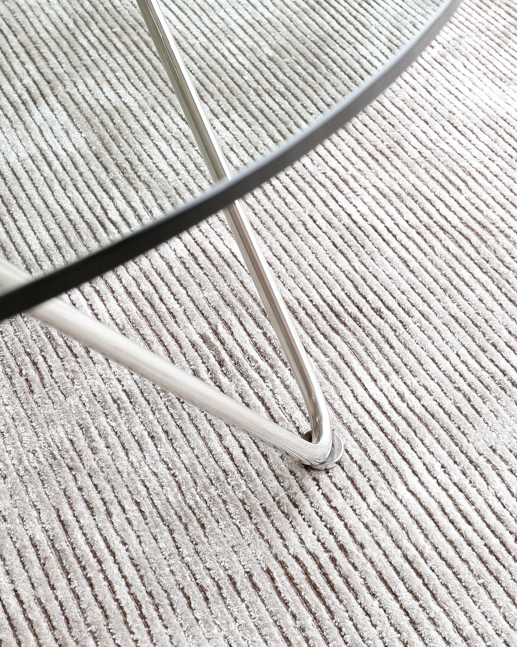 Partial view of a sleek, modern furniture leg with a chrome finish, set against a textured beige carpet.