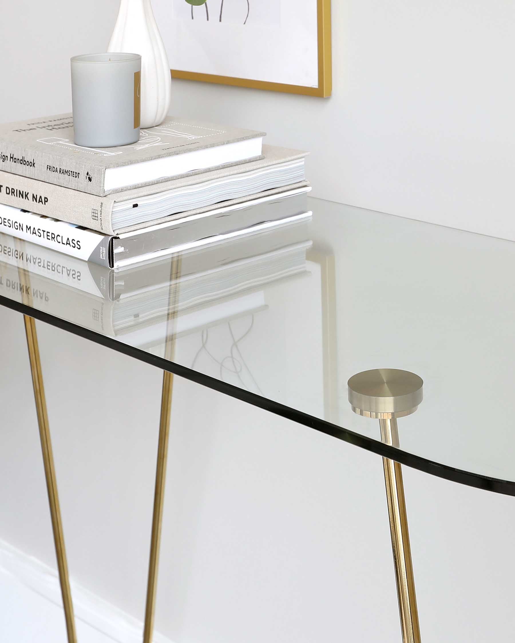 Modern minimalist console table with a transparent glass top and slim golden metal legs.